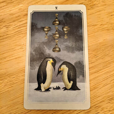 Picture of the Five of Cups tarot card. Card depicts two adult penguins crouching over a lifeless baby penguin. Above them are three goblets facing downward, and two facing upright.